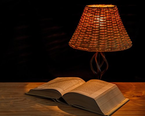 Cozy evening setup with a warm reading lamp shining over an open book and tablet